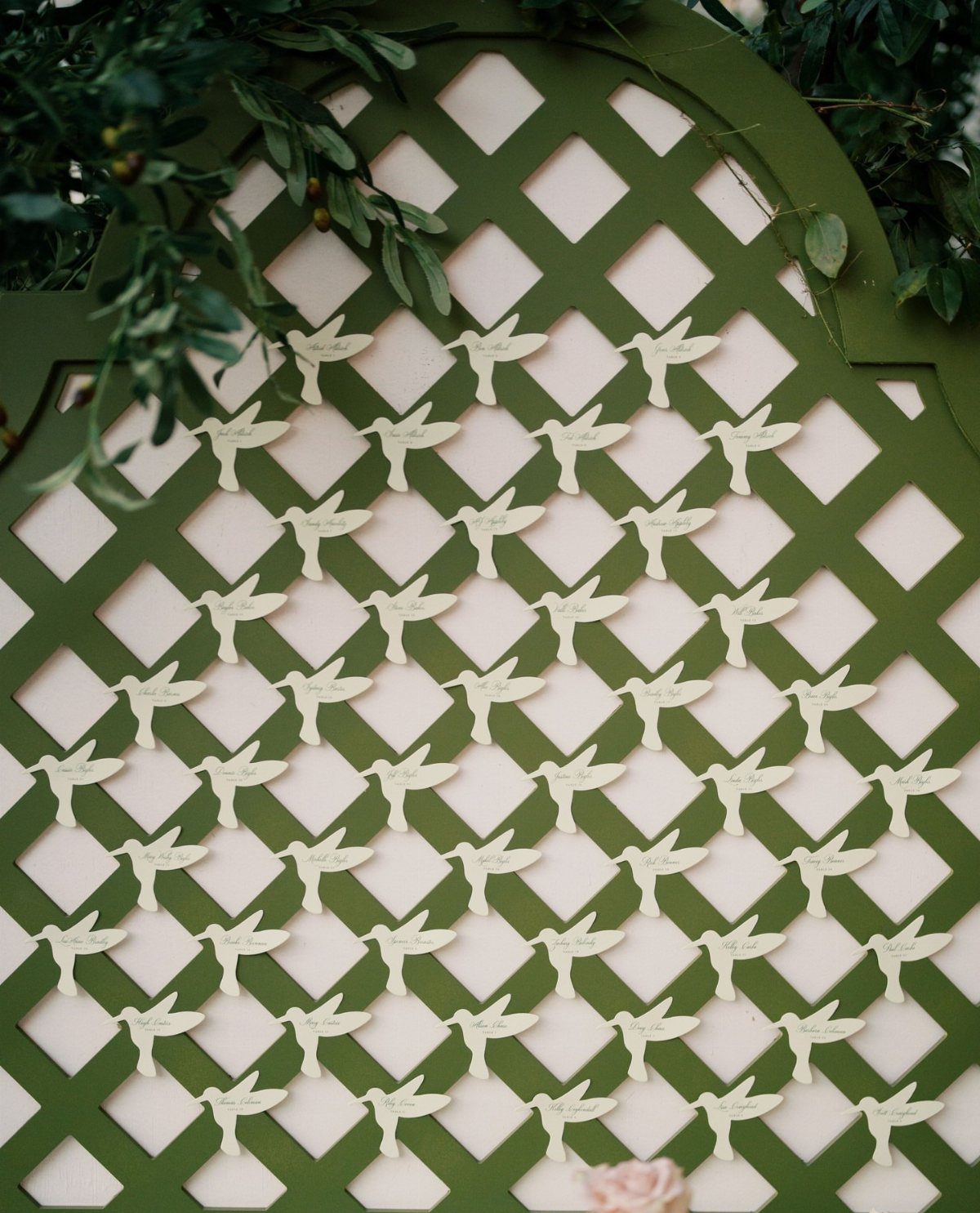 Green wooden lattice trellis with small white bird-shaped cards and green foliage.