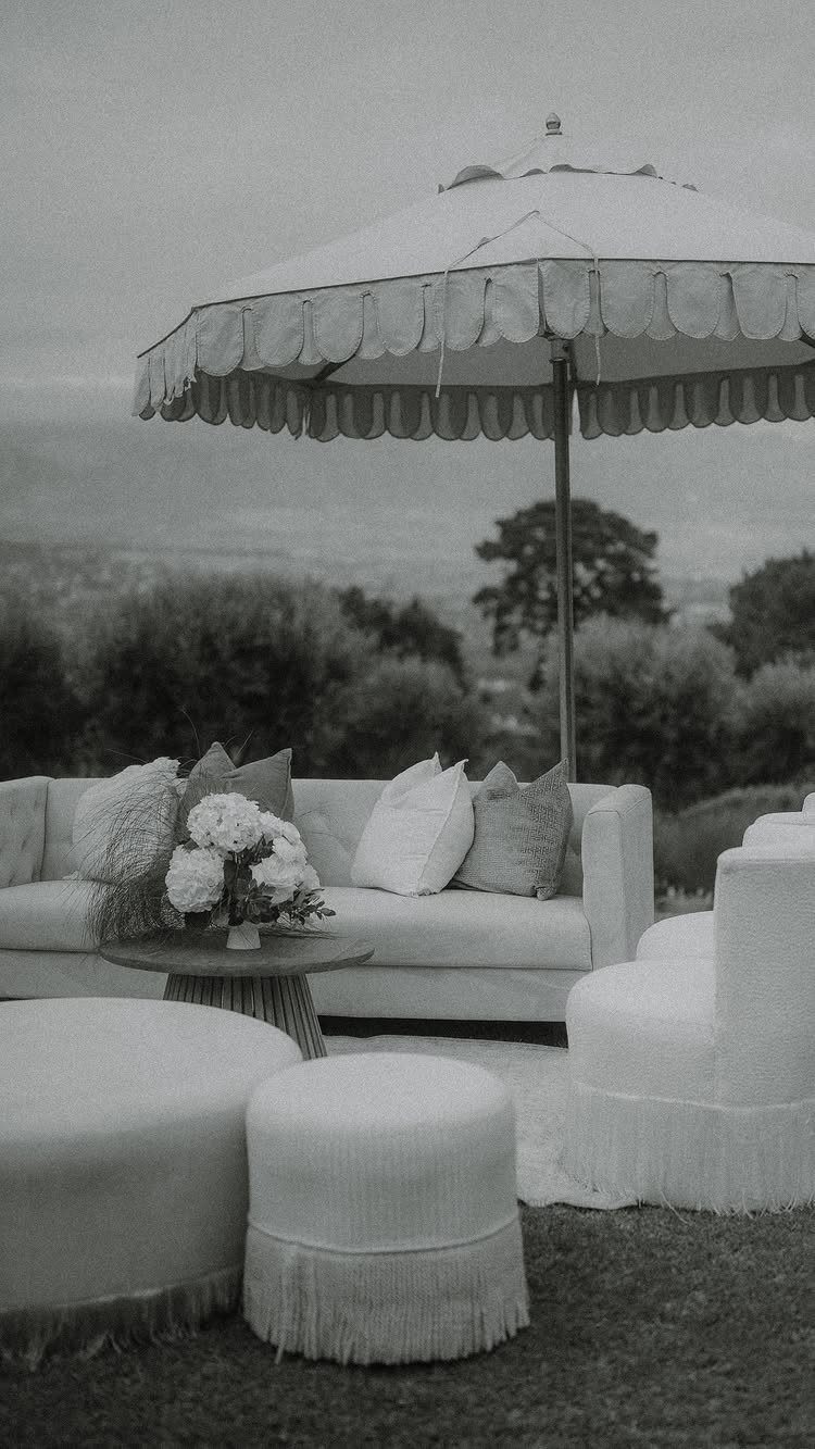Outdoor lounge area with white sofa, fringed ottomans, and a scalloped patio umbrella.