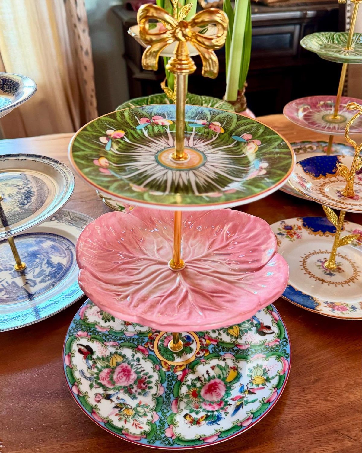 Three-tiered dessert stand with floral and pink shell plates on a wooden table.