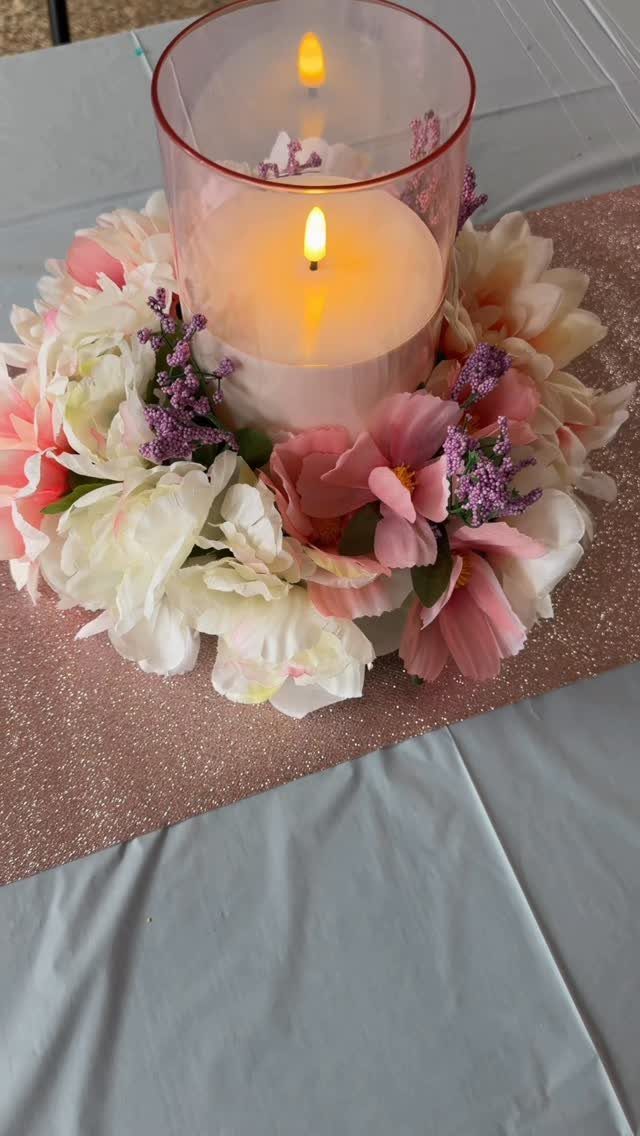 Lit pillar candle in glass cylinder surrounded by pink and white floral ring