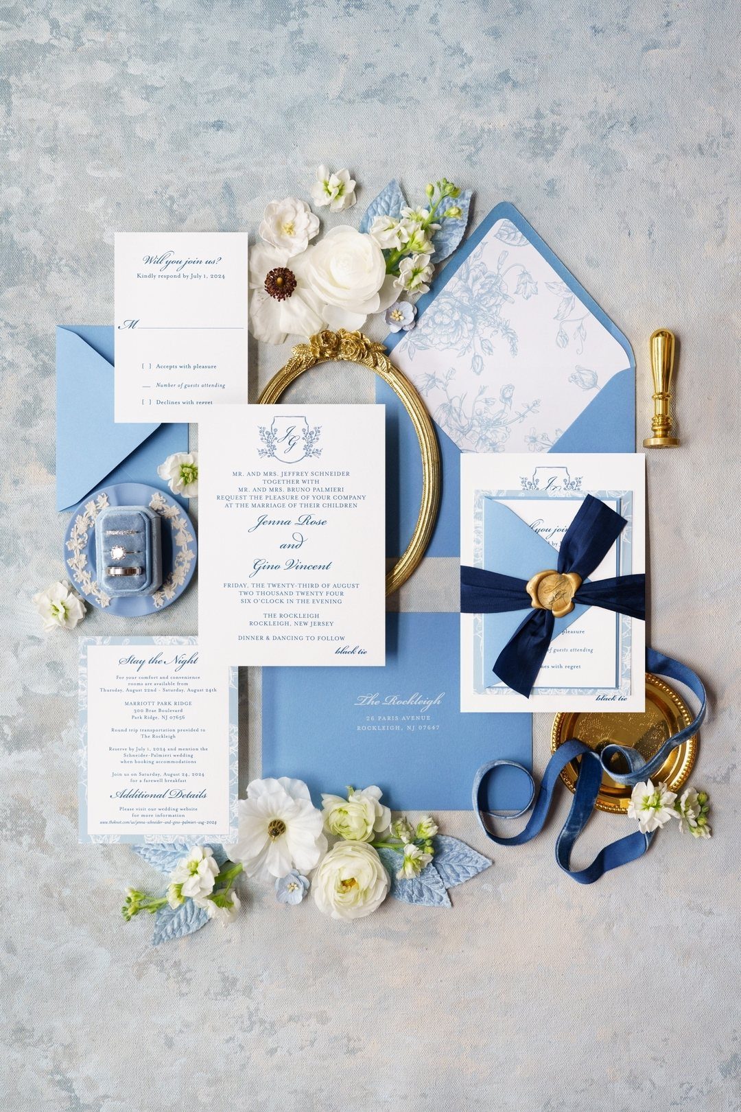 Wedding invitation suite with blue envelopes, navy ribbon, and white floral accents.