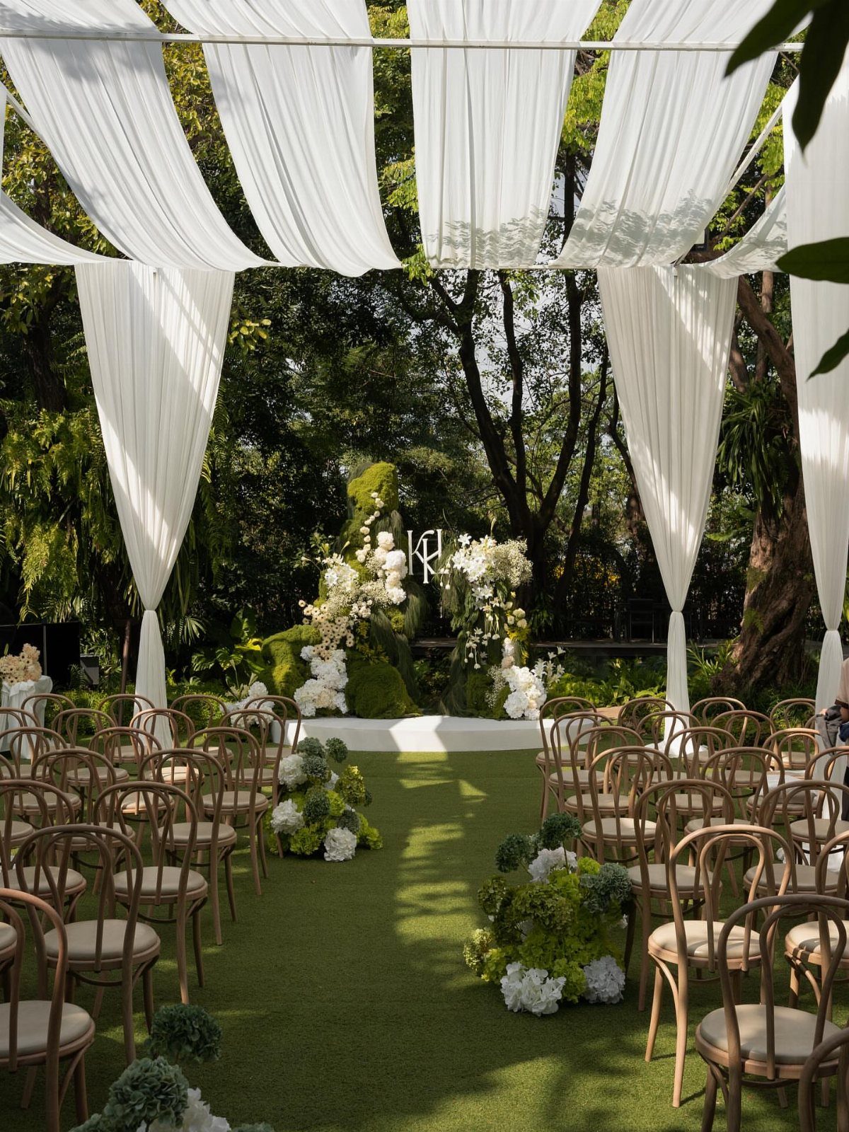 Outdoor wedding ceremony setup with white fabric draping and floral aisle decorations.