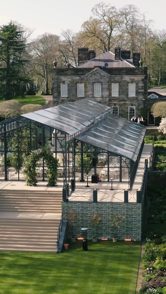 Glass marquee with black frame on a stone terrace near a manor house.