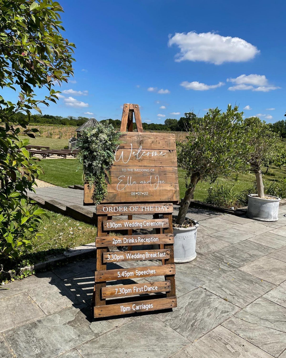 Wooden wedding welcome and order of the day signs on a stone patio.