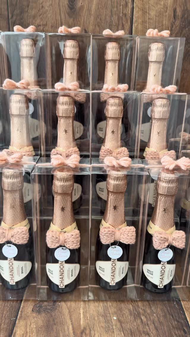 Small Chandon sparkling wine bottles with pink bows in clear packaging on wood.