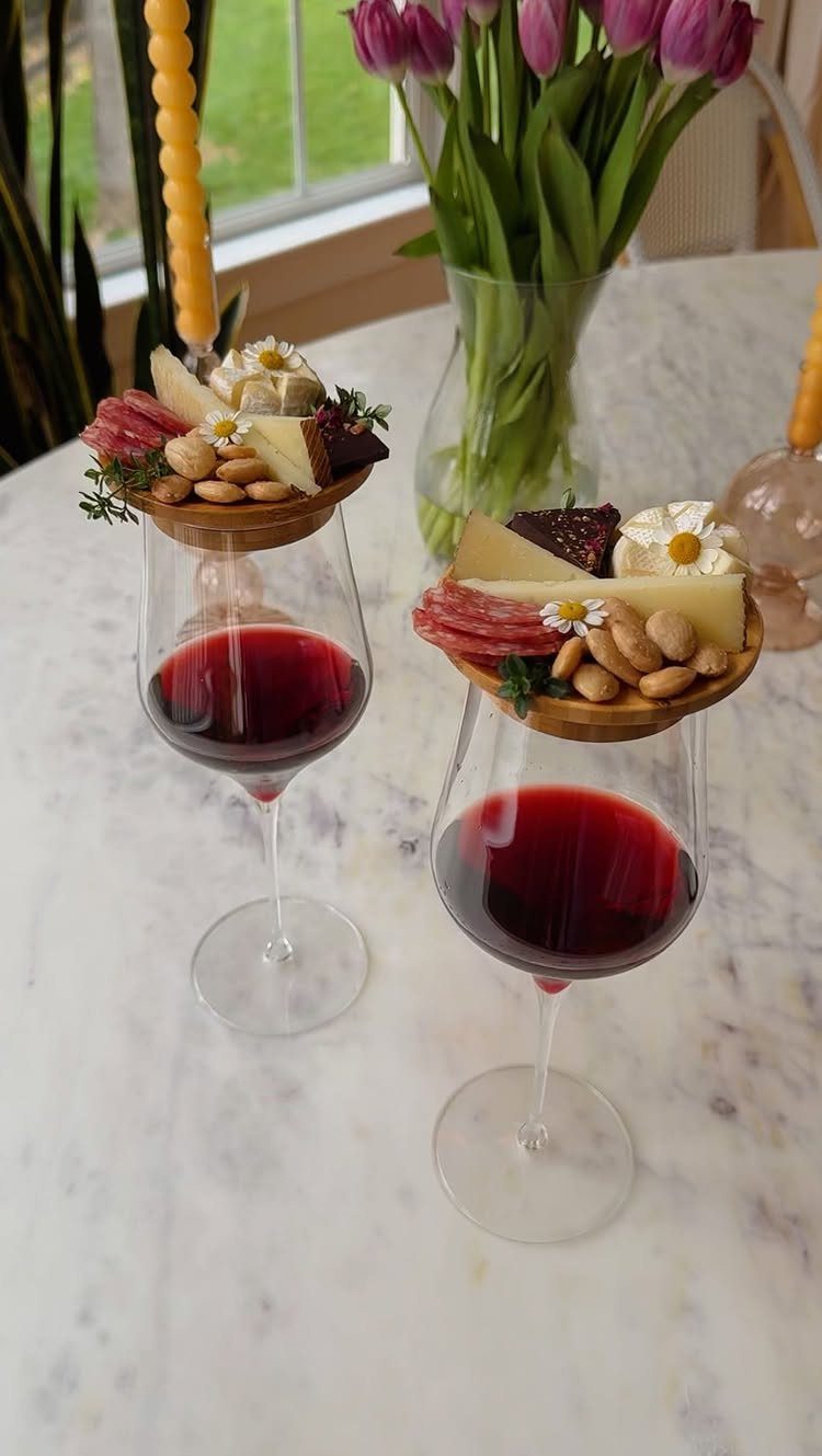 Wine glasses topped with charcuterie boards featuring cheese and meats on marble table