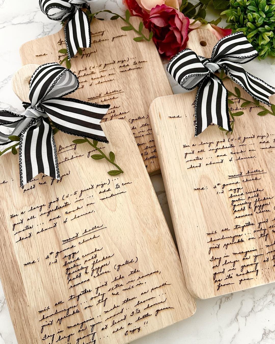 Wooden cutting boards engraved with handwritten recipes and tied with striped ribbons.