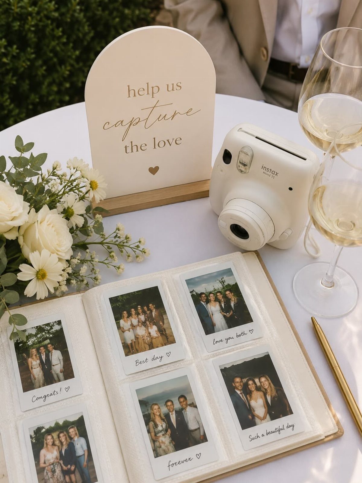 Open wedding guest book with instant photos, white camera, and white floral arrangement.