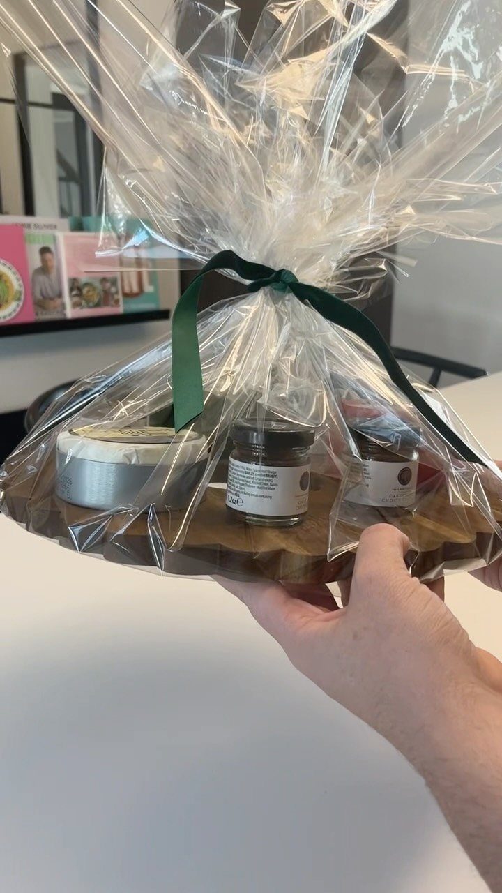 Wooden serving board with food jars wrapped in clear cellophane and green ribbon