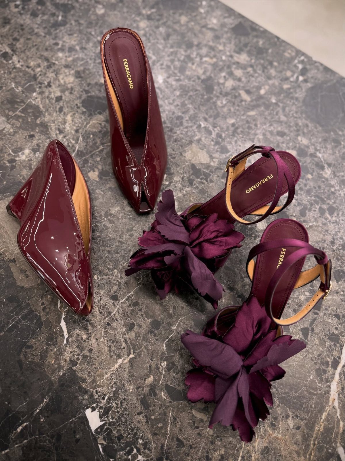 Burgundy patent leather pumps and strappy sandals with fabric flowers on marble surface