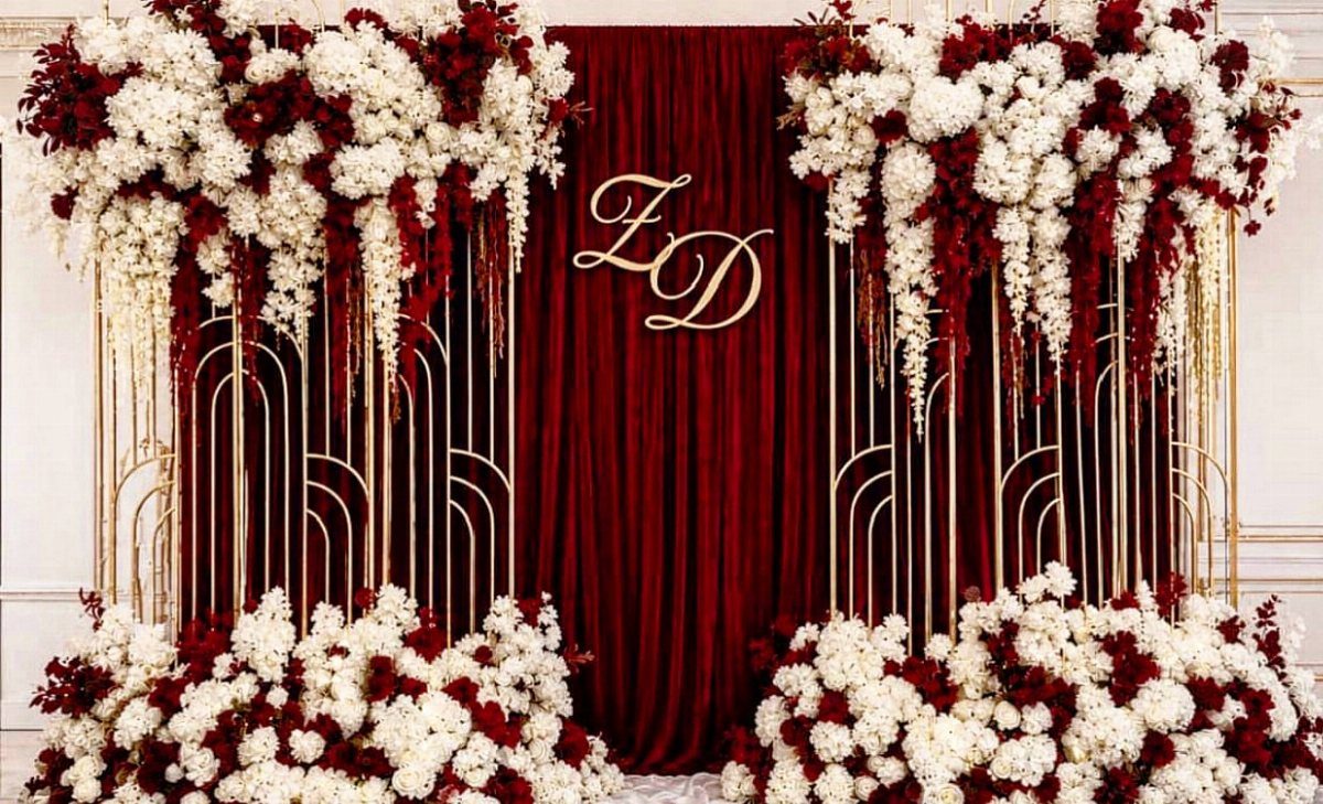 Burgundy velvet curtain and gold arched frames decorated with white and burgundy flowers.