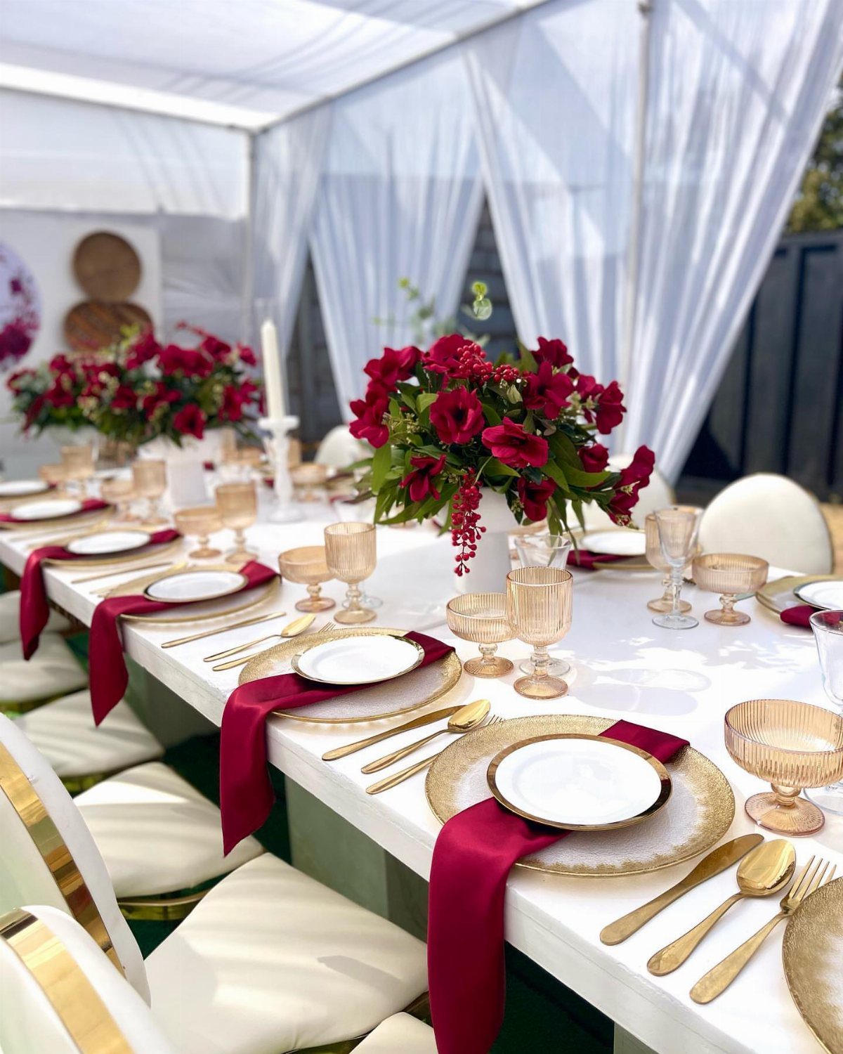 Wedding table setting with burgundy napkins, gold plates, and red floral centerpieces.