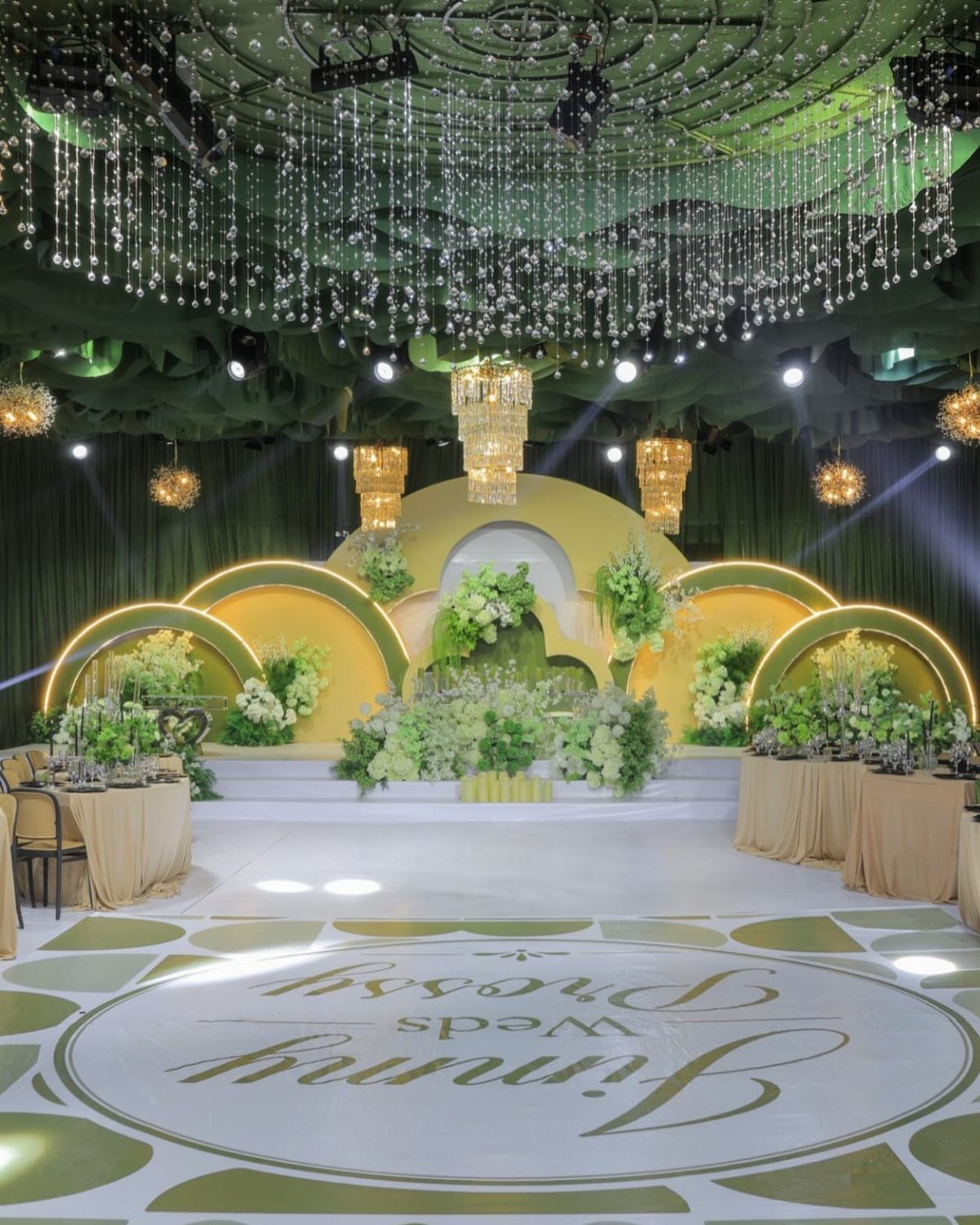 Lavish wedding venue with green drapes, gold arches, and white floral arrangements.