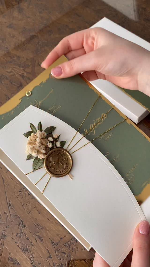 Green and gold wedding invitation with a gold wax seal and dried flowers.