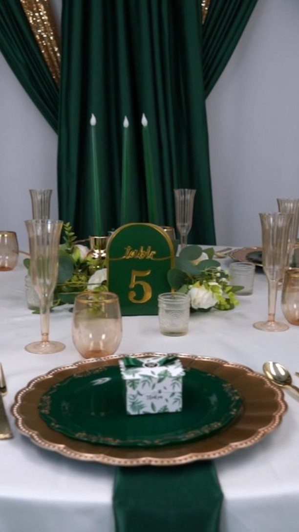 Emerald green and gold wedding table setting with plates, glassware, and floral centerpieces.