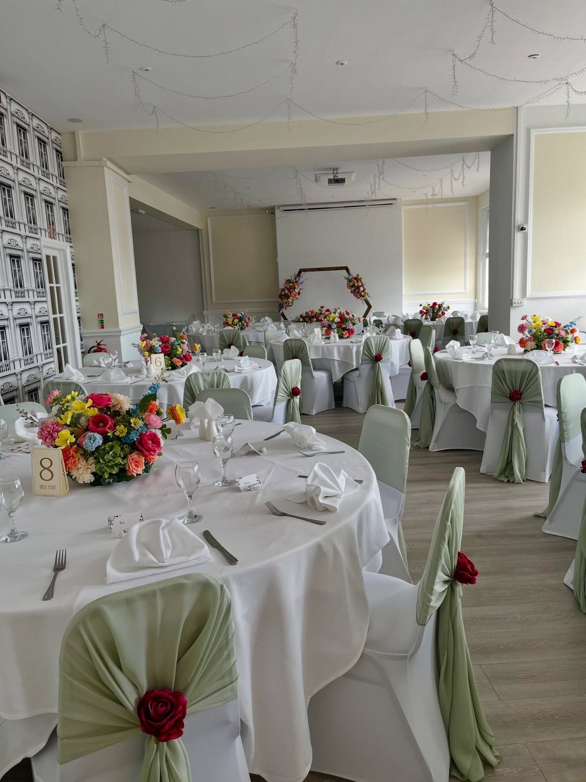 White wedding chairs decorated with sage green fabric sashes and red floral accents