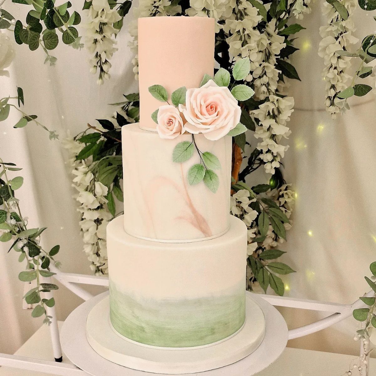 Three-tier wedding cake with pink and green accents and pink sugar roses.