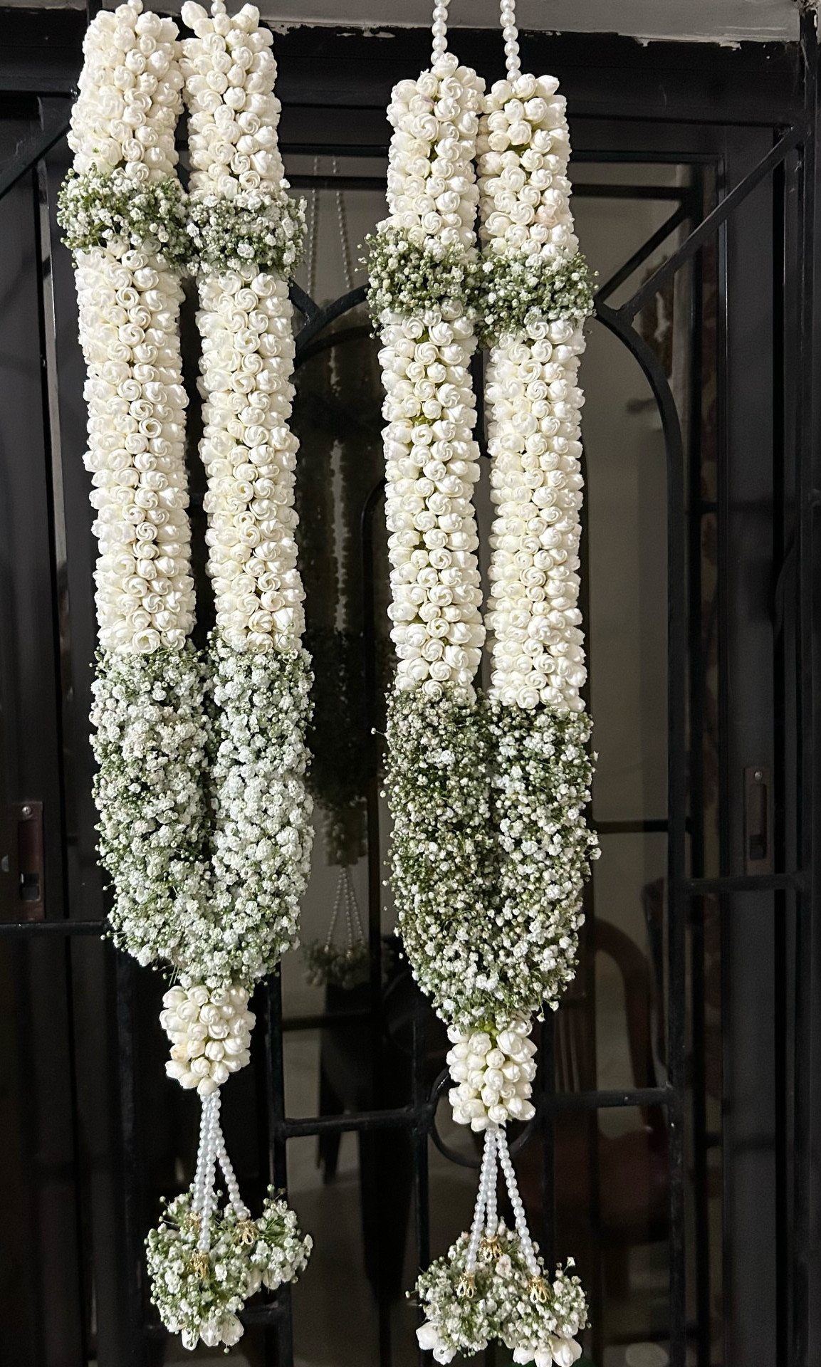 Two white and green floral garlands hanging vertically against a dark background.