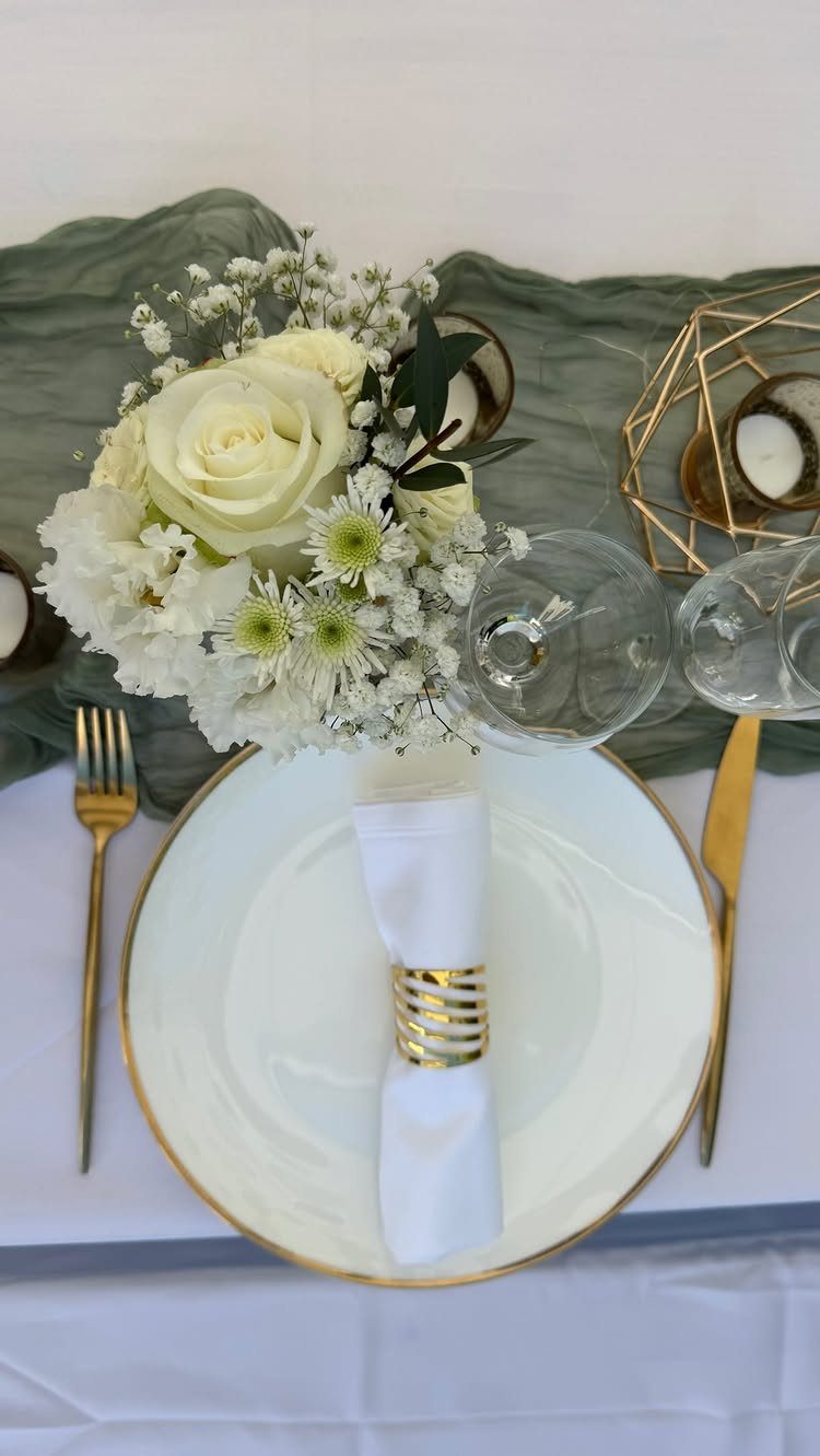 Wedding table setting with white roses, gold cutlery, and a sage green runner.