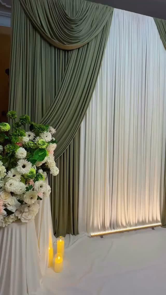 Olive green and white draped fabric backdrop with white floral arrangement and candles.
