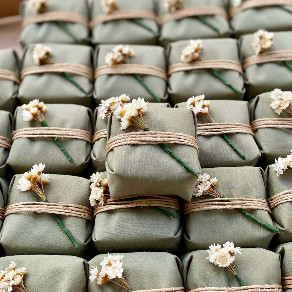 Sage green fabric wrapped gifts tied with brown twine and white dried flowers
