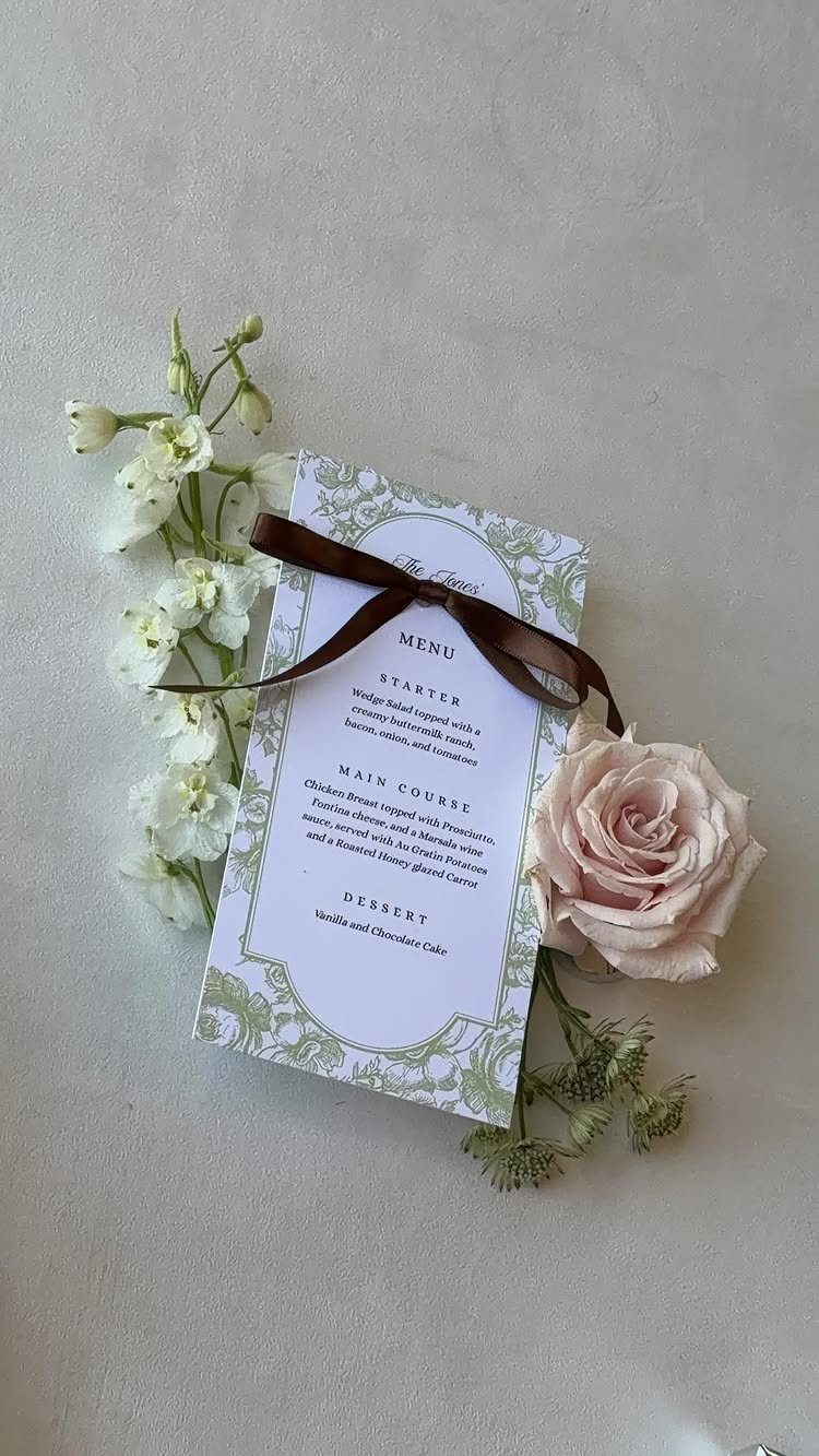 Wedding menu card with green borders, brown ribbon, and pale pink rose flower.
