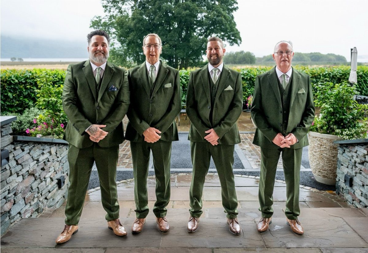 Four men in olive green wedding suits and brown shoes posing outdoors.