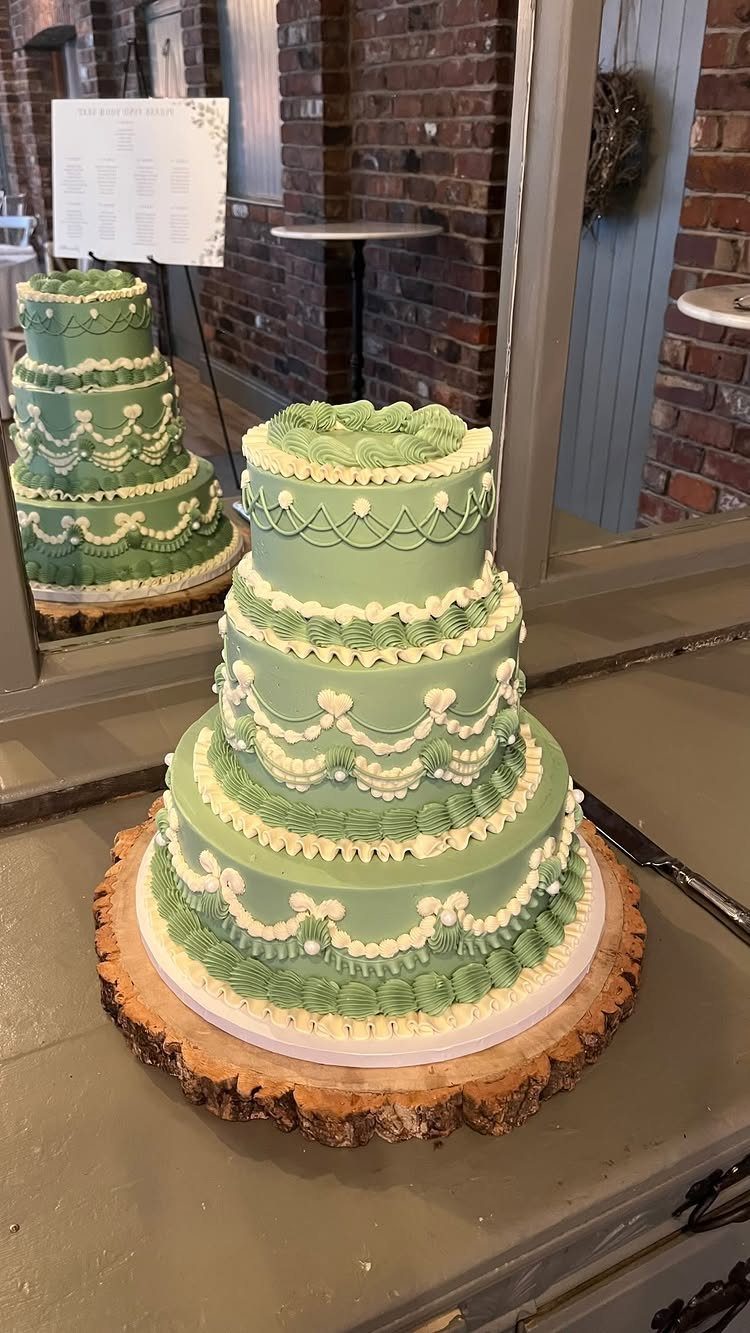 Three-tiered light green wedding cake with white frosting on a rustic wood slice.