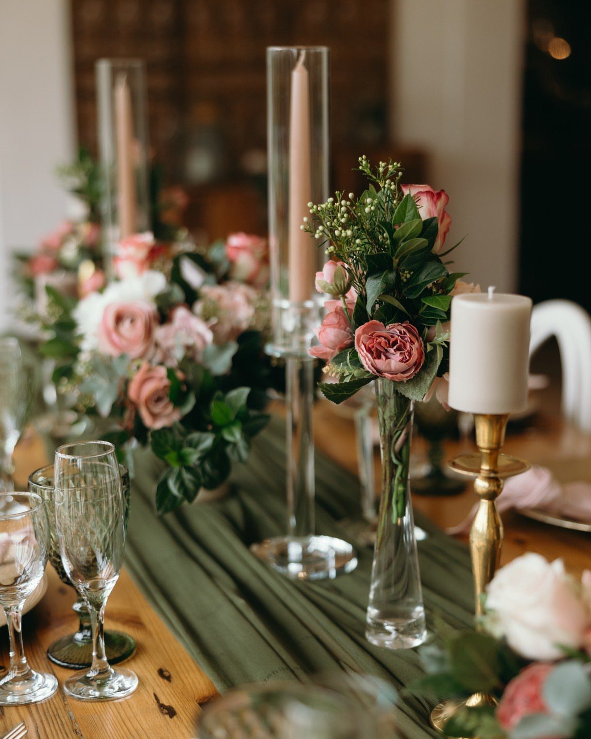 Wedding table setting with dark green runner and pink rose floral arrangements.