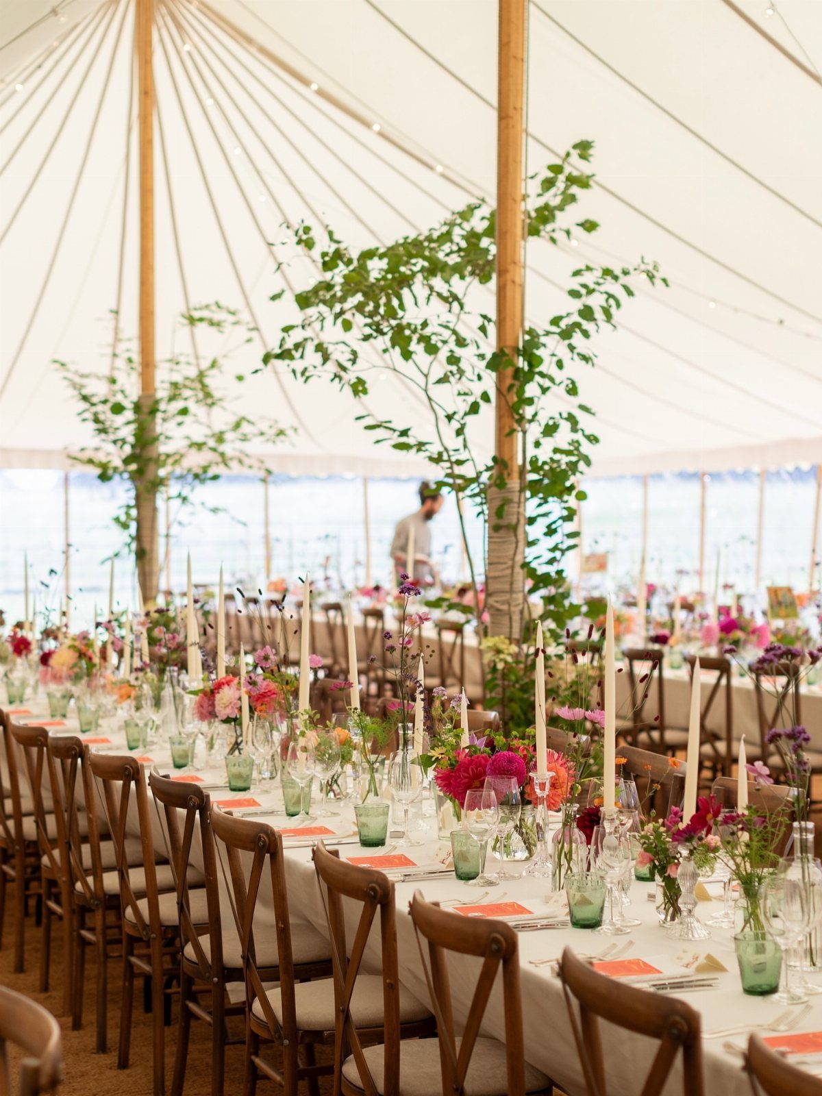 Wedding table setting with pink flowers and green accents inside a white tent.