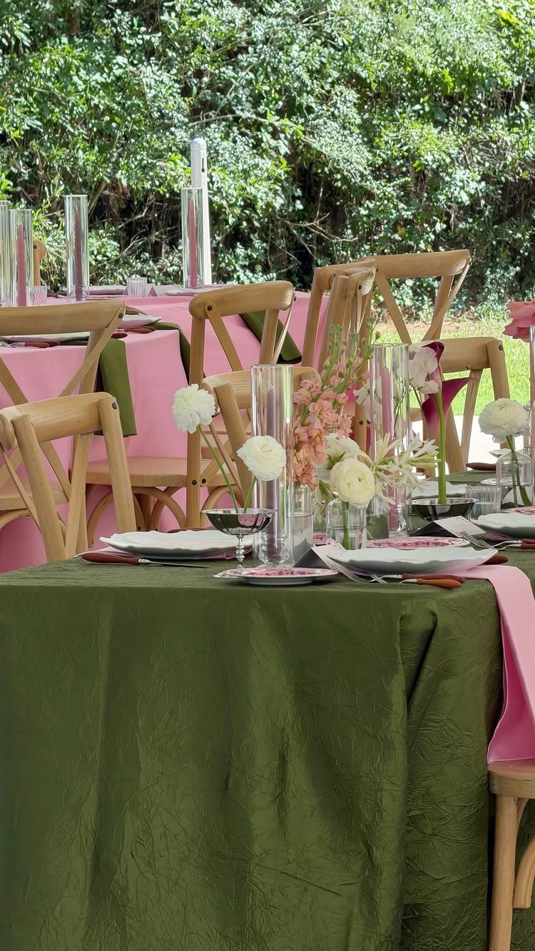 Olive green tablecloth and pink napkins with floral centerpieces at an outdoor wedding.