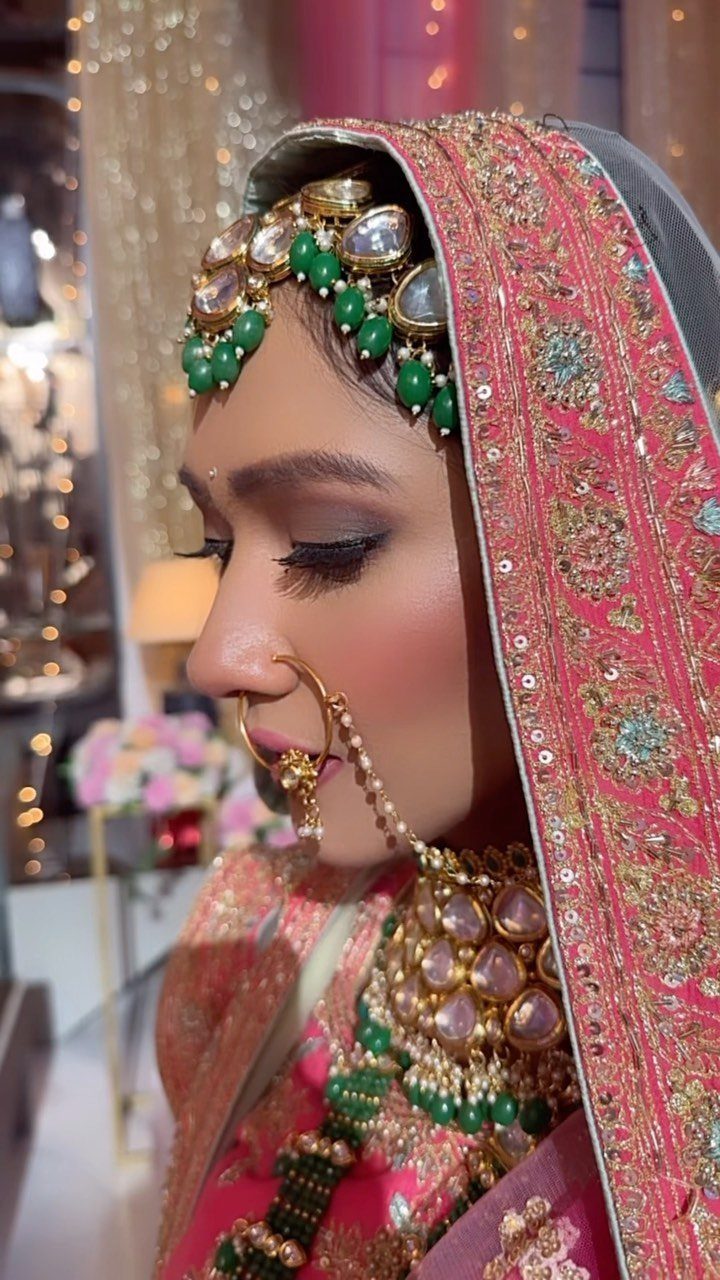 Bride in pink embroidered veil and gold jewelry with green bead accents.