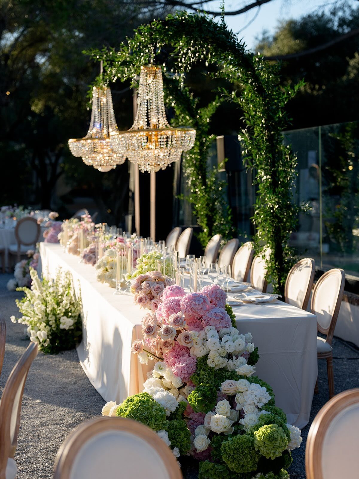Wedding reception table with pink and green floral arrangements under crystal chandeliers.