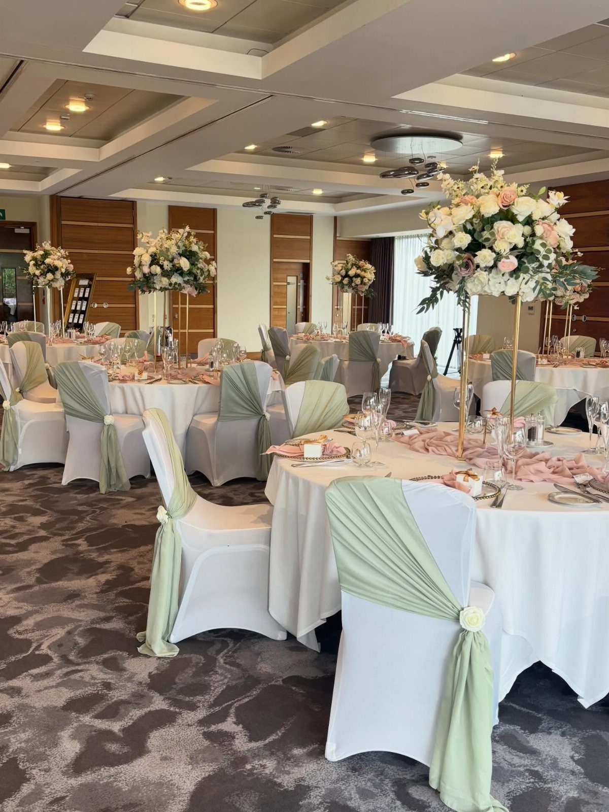 Wedding reception tables with white linens, pale green chair sashes, and pink floral centerpieces.