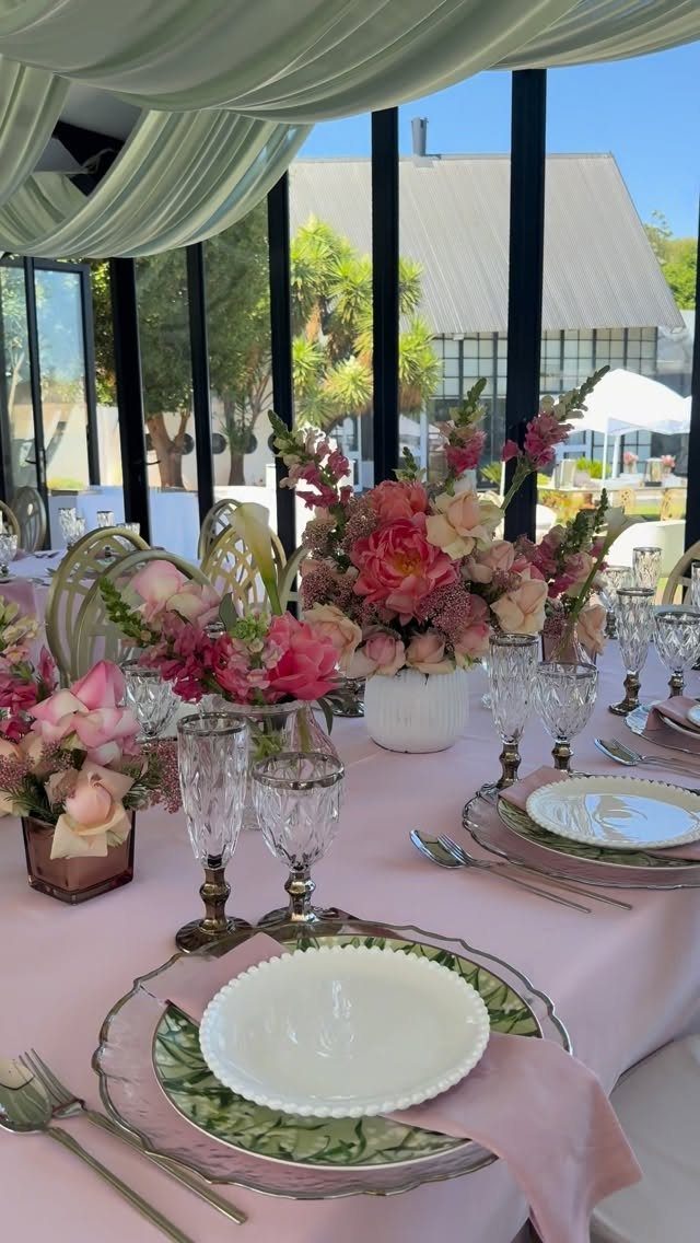 Wedding table setting with pink tablecloth, peach flowers, and green foliage accents.