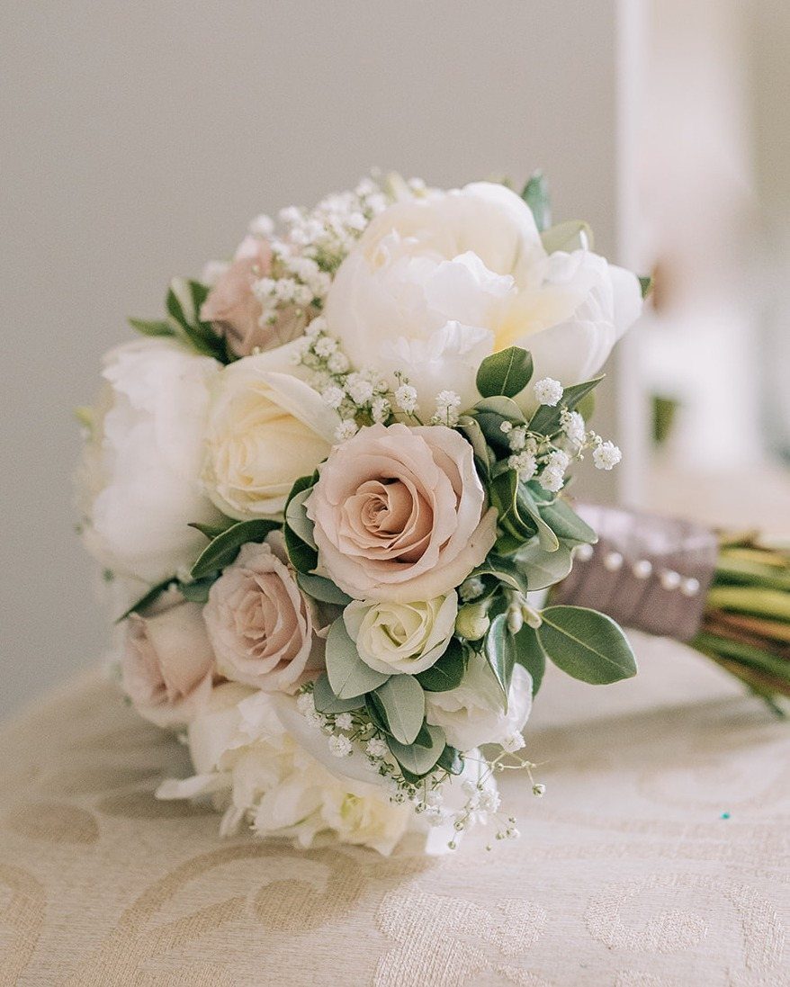 Bridal bouquet with pale pink and white roses, baby's breath, and green foliage.