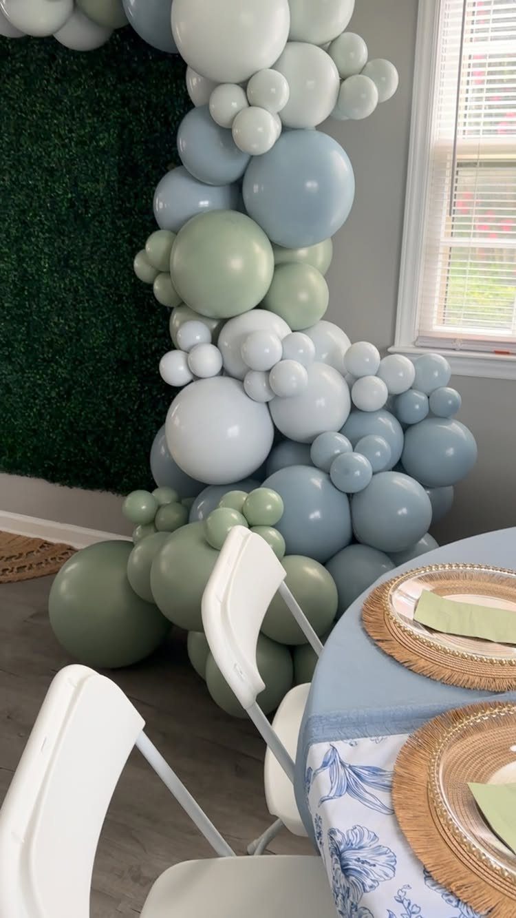 Balloon arch in sage green and dusty blue next to a decorated table.