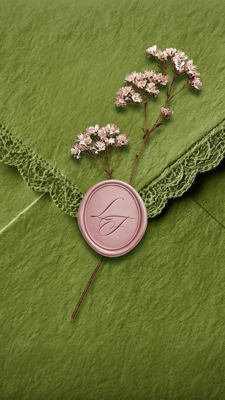 Sage green envelope with lace trim, dusty rose wax seal, and dried pink flowers.