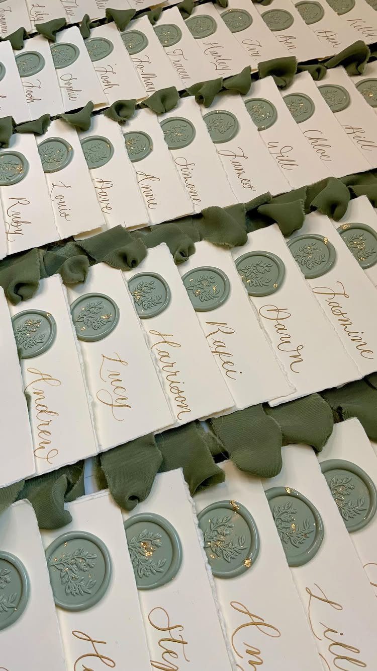 White place cards with gold calligraphy and sage green wax seals on fabric.