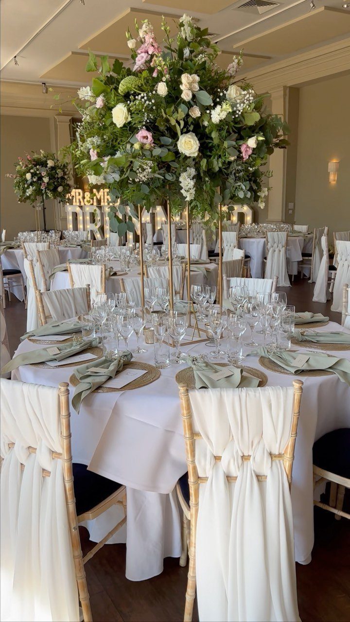 Wedding table setting with sage green, pink, and white flowers on gold stands.