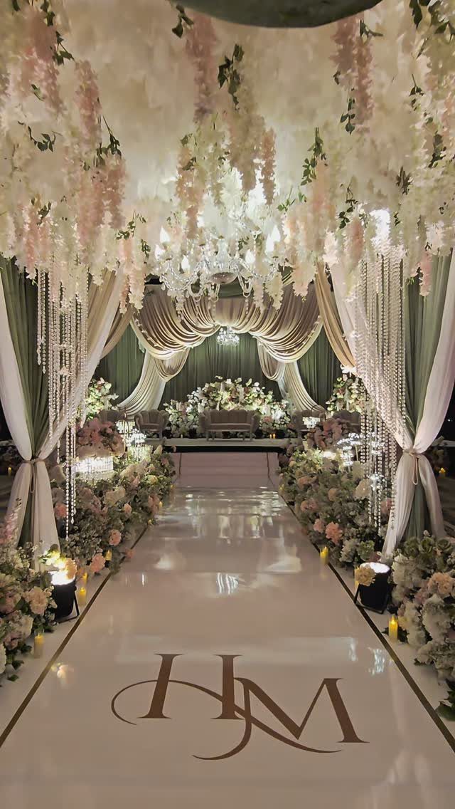 Wedding aisle with sage green drapes, pale pink flowers, and a gold monogram.