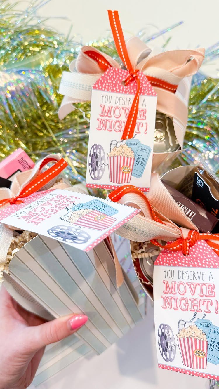 Gift bags with movie night tags and pink ribbons against green tinsel background