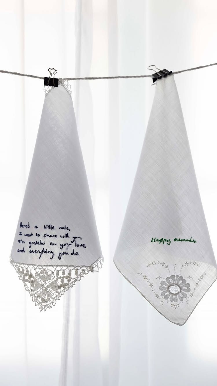 Two white handkerchiefs with handwritten notes and floral embroidery hanging on a wire.