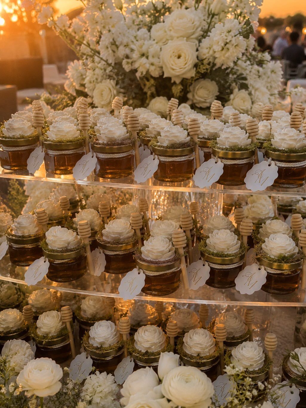 Small honey jars with white roses and honey dippers on acrylic shelves