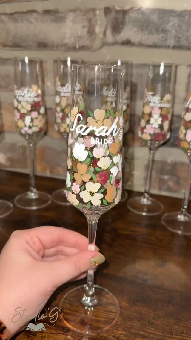 Champagne flute with painted colorful flowers and the name Sarah Bride on it.