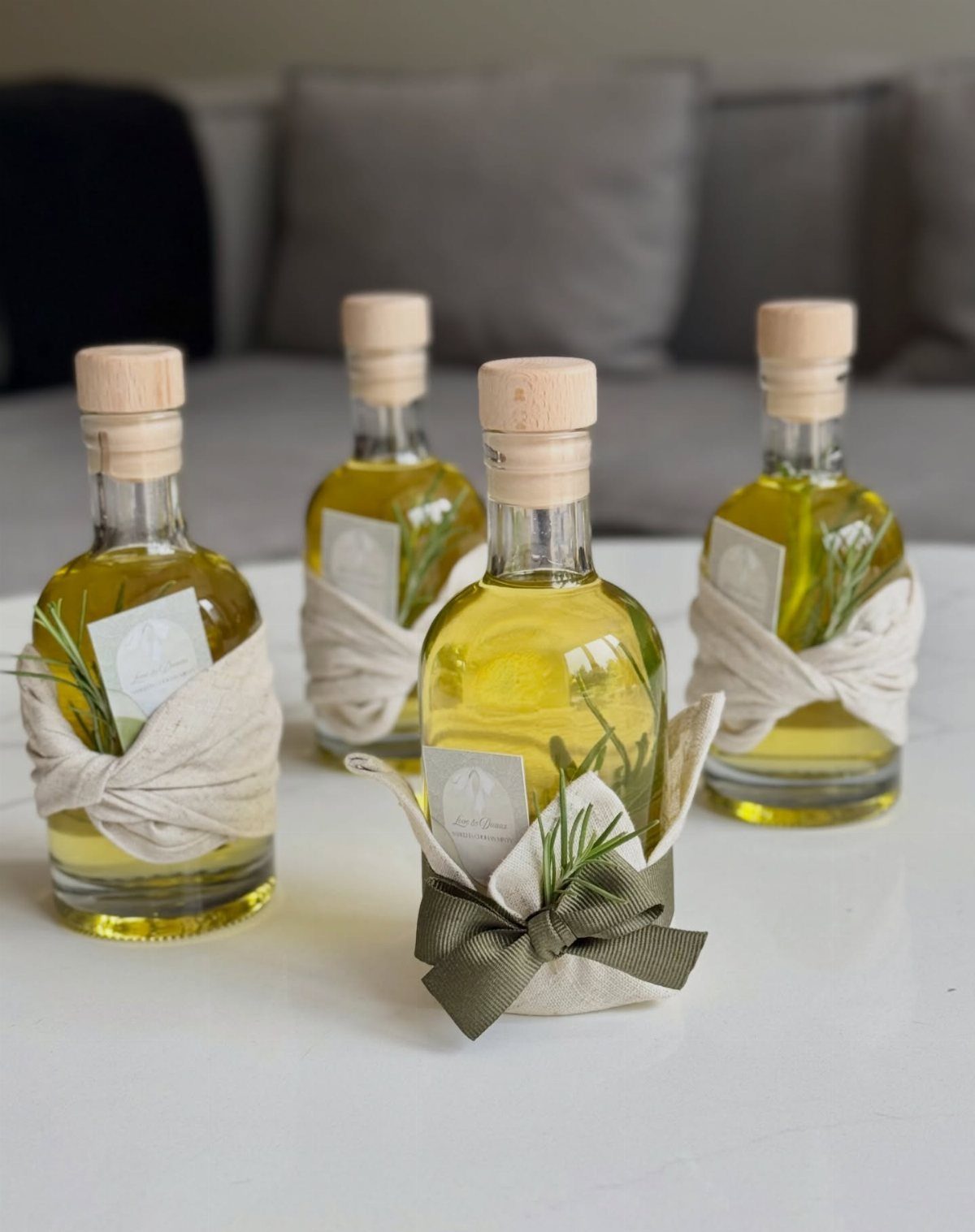 Four small olive oil bottles with rosemary, wrapped in white fabric and bows.