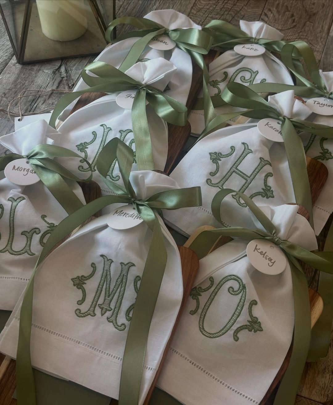 Monogrammed white tea towels tied with green ribbons on wooden boards.
