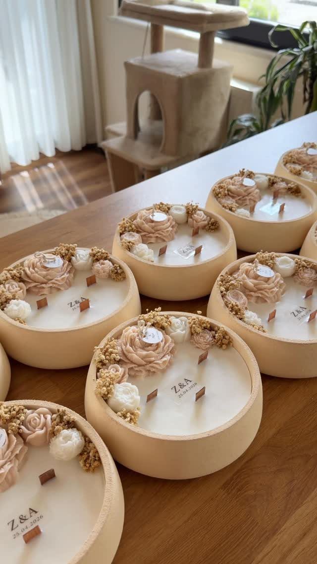 Cream-colored candles decorated with wax flowers and personalized initials on a wooden table
