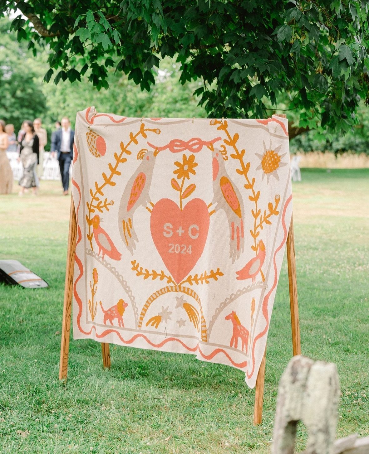 Woven cream blanket with orange bird illustrations and a heart on a wooden easel.