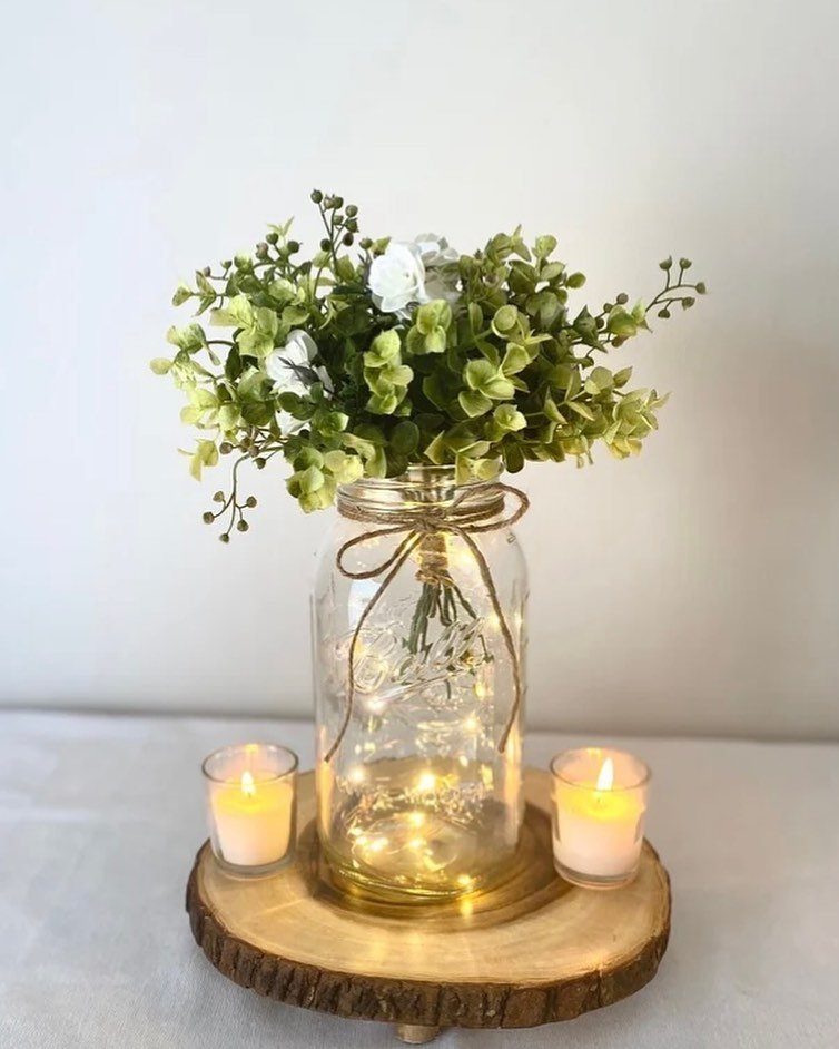 Decorated mason jar with fairy lights and flowers on a wooden slice base